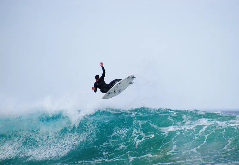 Surfer launching an aerial on a MAT surfboard over a turquoise wave